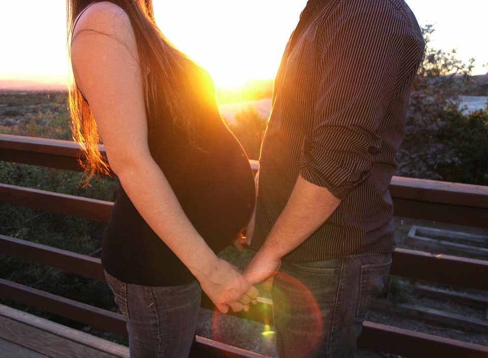An expectant couple holding hands at sunset